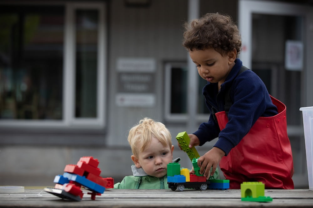 Två barn leker med duplo tillsammans utomhus.