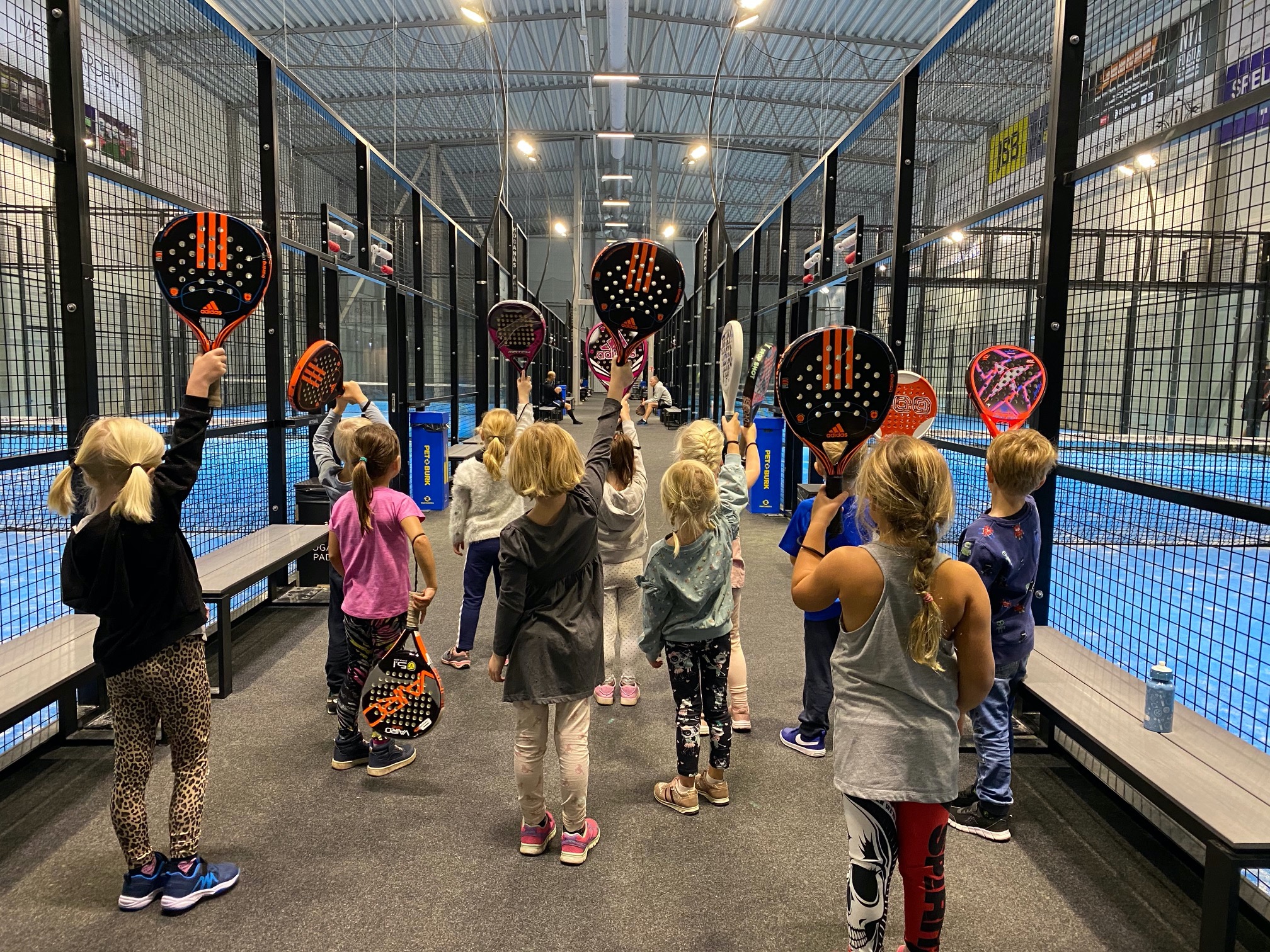 Barn i en padelhall håller upp sina rack.