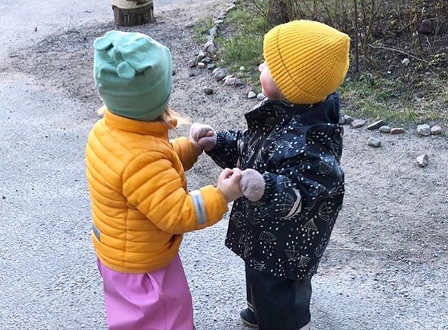 Barn i regnkläder håller varann i händerna ute på gården.