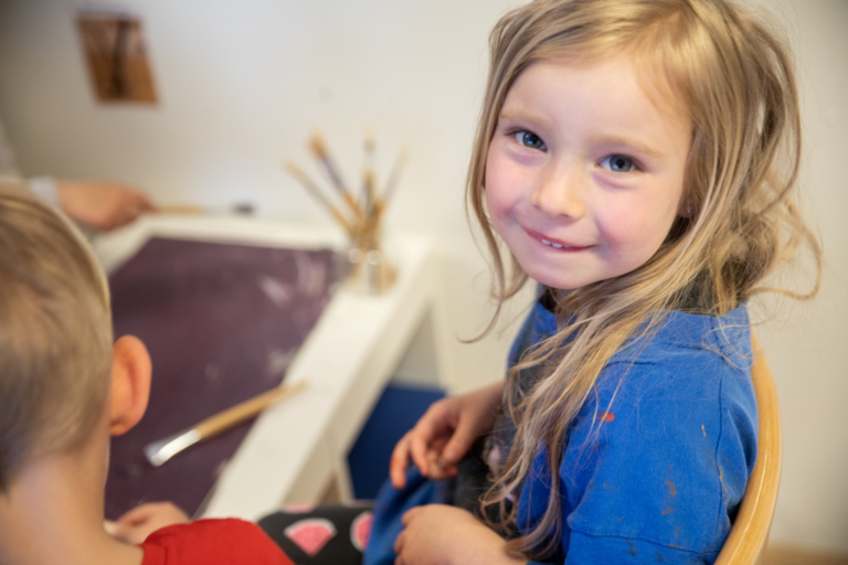 Blond flicka målar och tittar in i kameran