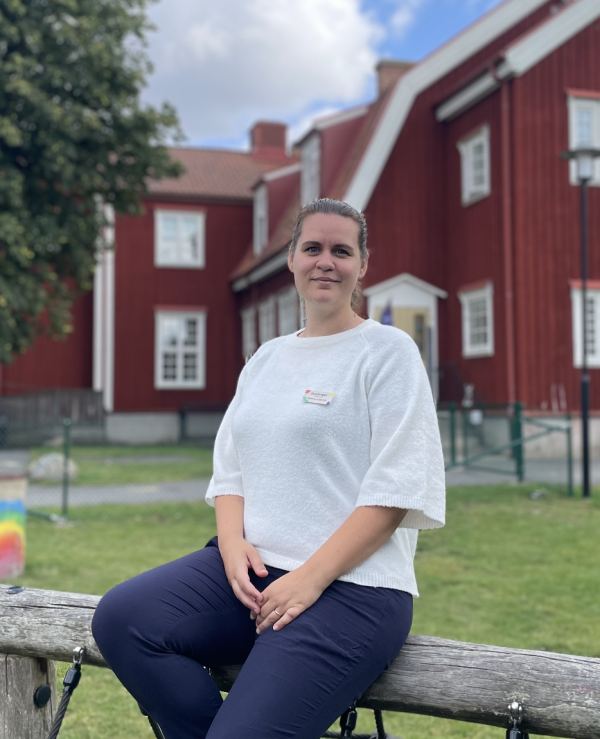 Rebecca sitter framför förskolans gård och ler in i kameran.