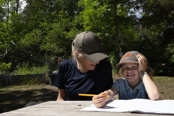 Leende pedagog och barn sitter vid ett bord utomhus
