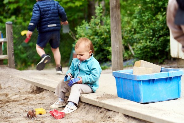 ett sittande barn leker med leksaker i sandlåda