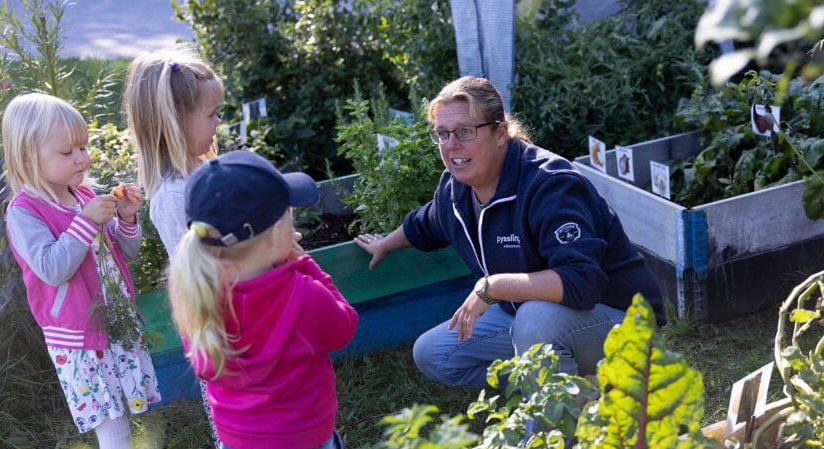 Pedagog och barn bland odlingslådor på förskolan