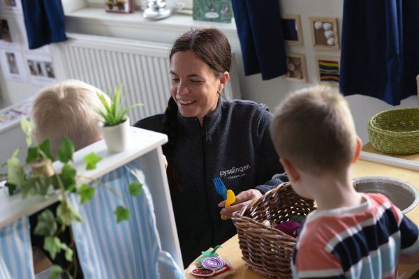 leende pedagog sitter på golvet och leker med barn