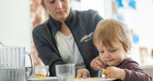 Barn som äter med händerna under överseende av en pedagog