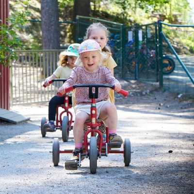 tre glada barn cyklar på förskolans gård