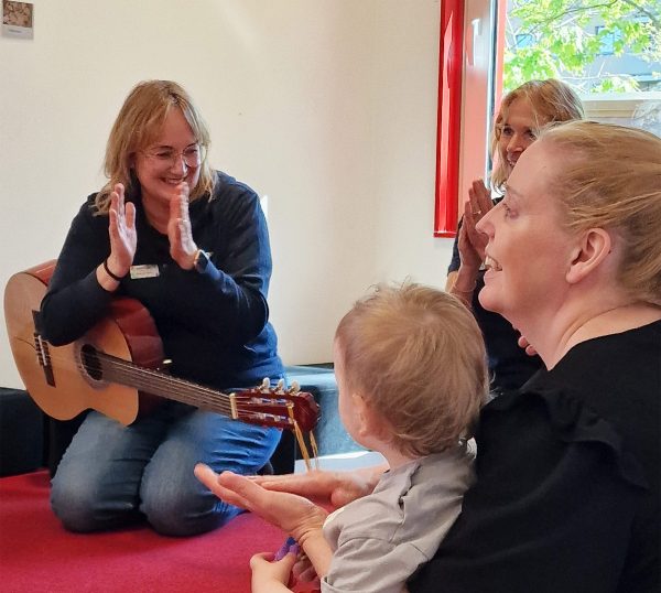 Vuxna och ett barn sitter i ring och sjunger och klappar