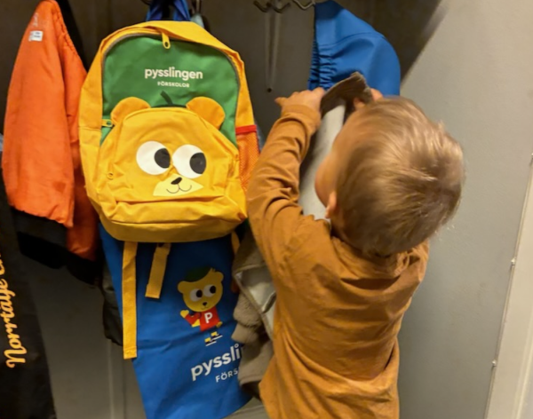 Barn hänger upp jacka i hallen.