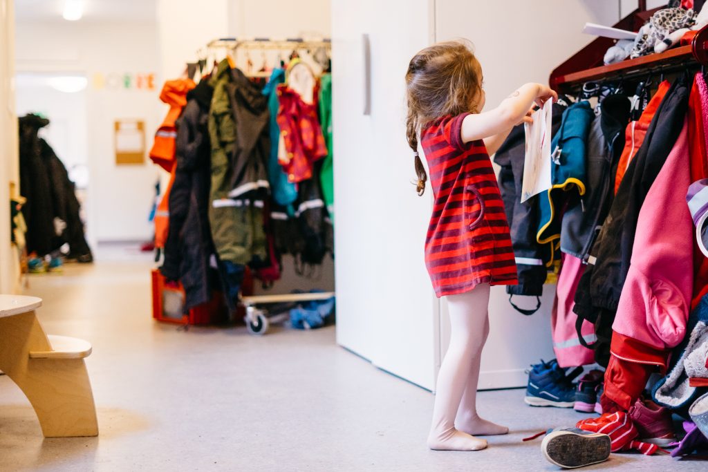 Flicka hänger upp kläder på förskolan