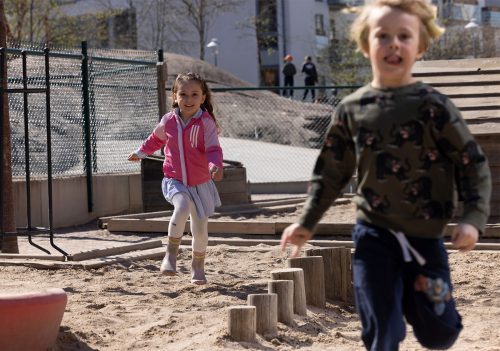 två leende barn springer i sanden på förskolegård