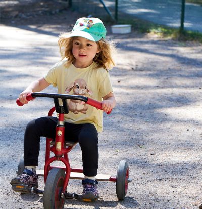 Barn cyklar på trehjuling på förskolans gård