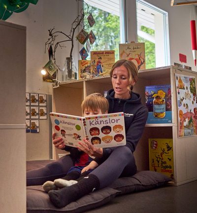pedagog sitter med ett barn i en läshörna och läser tillsammans