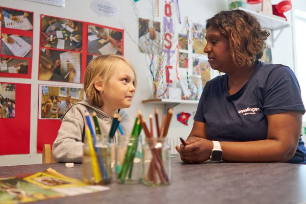 barn och pedagog sitter vid ett bord och ser på varandra i en kreativ lärmiljö