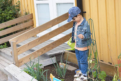 pojke som står i rabatt och vattnar växter med vattenkanna