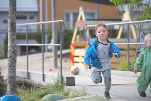 pojke i blå jacka som springer på förskolans gård