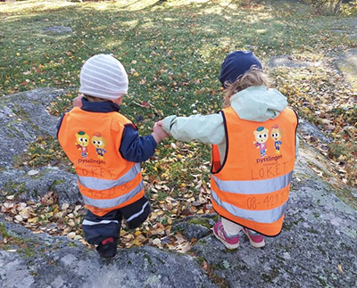 två barn håller hand och går ute i naturen på förskolan