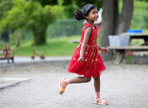 flicka i röd klänning springer ute på en förskolegård