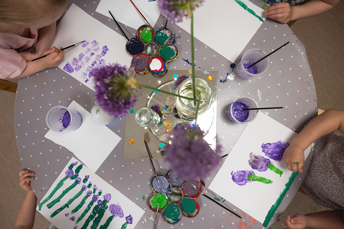 barnhänder som målar lila blommor utifrån stilleben kring ett runt bord